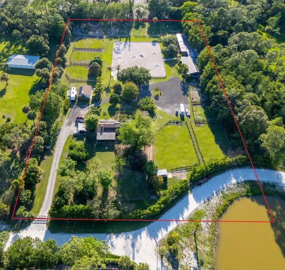 Aerial photograph of the farm with the property boundary outlined in red: a covered barn and arena to the north, the house and paddocks at the centre, mature trees around the edges, and a canal along the southern boundary.